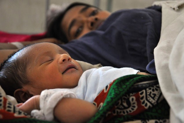 Photo of a newborn baby with the mother lying in the background
