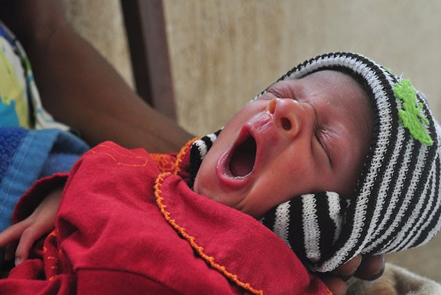 A newborn baby yawns while being held