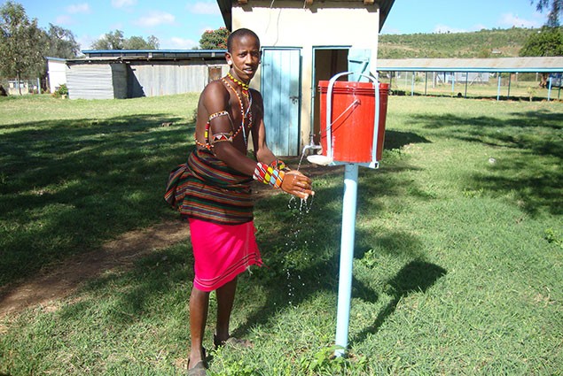 A Maasai man washes his hands from a suspended buicket of water