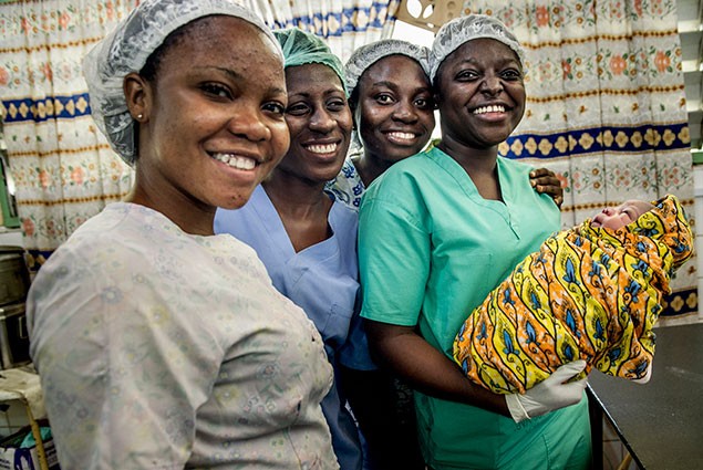 Health workers smile at the camera while holding a new born baby.