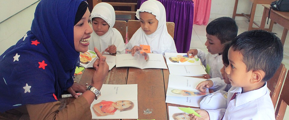 Guru dan murid melakukan praktik membaca menggunakan buku bacaan berjenjang dari USAID