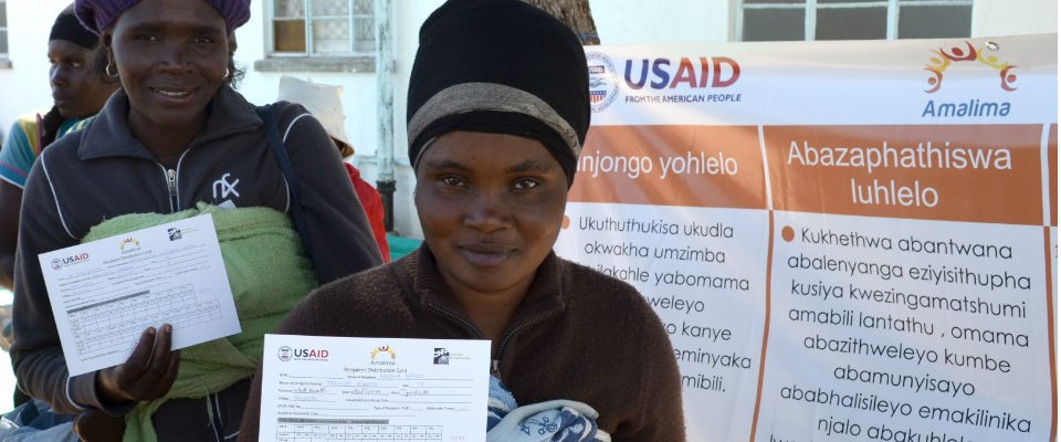 Mothers hold up their ration cards at a distribution site in Matabeleland South Province. USAID provides rations of fortified co