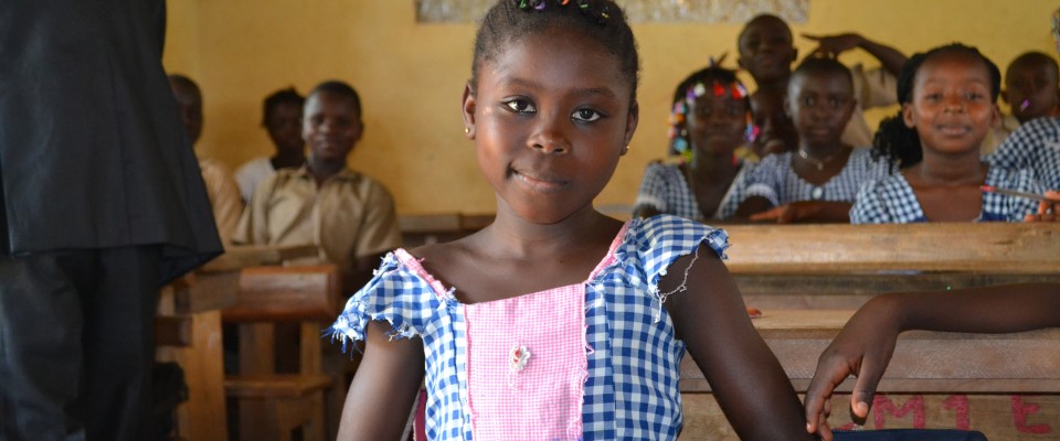 Une écolière avec un sourire au coin assise sur un banc dans une salle de classe