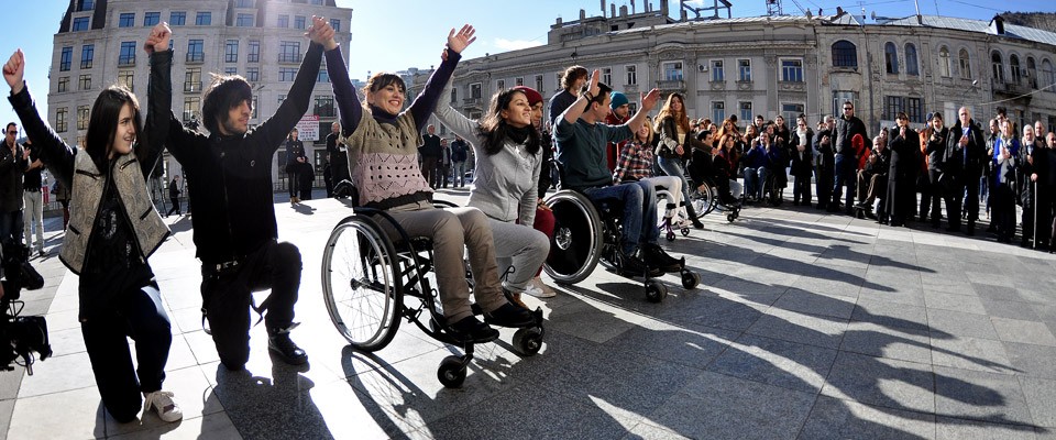 People holding hands, kneeling and in wheelchairs.