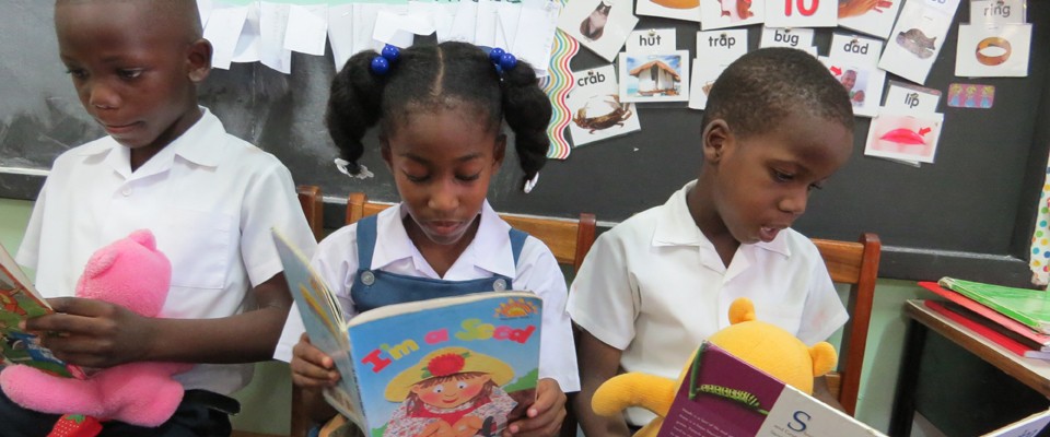 These kindergarten students from the Seventh Day Adventist Primary School in Grenada, seen reading while holding their 'reading buddies' have already benefitted from USAID's Early Learners program.