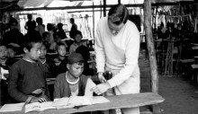 Meo tribe children and Hal Freeman, right, look at textbooks provided by USAID in Laos. In the background, a parachute serves as