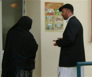 Using an Access to Justice Campaign poster, a USAID worker explains women’s right to inheritance to a woman entering a health cl