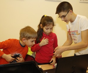 Andrei Copaci îndrumă doi copii în procesul de construire a unui robot, în cadrul EU Robotics Demo Day 