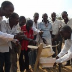 The men of the Asisizaneni Community Health Club demonstrate how to use a tippy tap for hand washing.