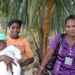 A woman holds a baby while standing with her female community health worker.