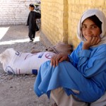Naz Gul sits outside school in her village of Chaghai with her monthly ration of wheat for her family.