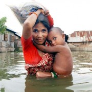 A mother carries her child in one hand and a packet of collected food in the other down a flooded road on the outskirts of Dhaka