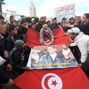 Tunisians from the Kasserine region walk with a Mohammed Bouazizi poster and the national flag in front of the government palace