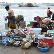 Displaced women try to wash their belongings, while a boat arrives with more flood victims I Gaza Province, Mozambique.