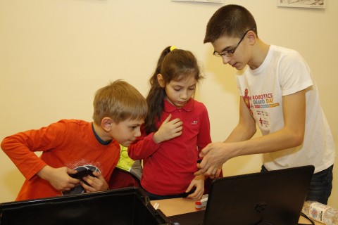 Andrei Copaci îndrumă doi copii în procesul de construire a unui robot, în cadrul EU Robotics Demo Day 
